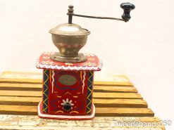 Charming vintage red coffee grinder with ornate designs, polished metal bowl, and functional drawer.