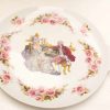 Elegant decorative plate featuring pink roses and 18th-century figures, perfect for collectors.