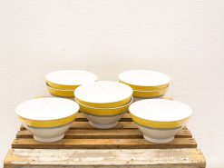 Set of six elegant white ceramic bowls with vibrant yellow rims on rustic wood.