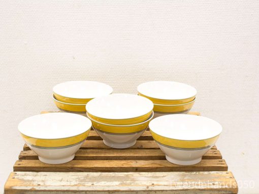 Set of six elegant white ceramic bowls with vibrant yellow rims on rustic wood.