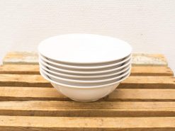 Stylish stack of white ceramic bowls on a rustic wooden surface, perfect for any meal.