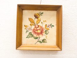 Vintage floral artwork in warm wood frame, featuring a rose and vibrant leaves.