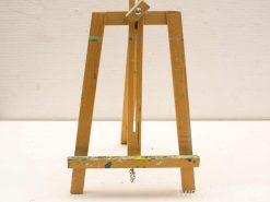 Light wooden easel with paint splatters, adjustable clamp, perfect for artists and creative projects.