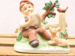 Vintage porcelain figurine of a joyful boy with his playful dog in nature.