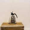 Elegant stainless steel coffee pot on rustic wood, blending modern style with rustic charm.