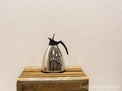 Elegant stainless steel coffee pot on rustic wood, blending modern style with rustic charm.