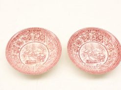 Vintage red transferware plates featuring charming pastoral scenes and scalloped rims.