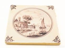 Vintage ceramic tile featuring a serene waterfront scene with a sailboat and intricate designs.