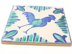 Whimsical blue rooster tile surrounded by green leaves, perfect for decorative or functional use.