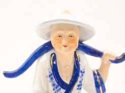 Charming porcelain figurine of an elderly man with blue floral accents and conical hat.