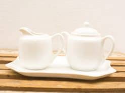 Elegant white porcelain tea set with cream jug and sugar bowl on curved tray.