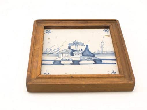 Rustic decorative tile featuring a serene blue landscape with a charming house and water lines.