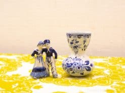 Charming Delft blue couple and vase set against vibrant yellow backdrop for stylish decor.