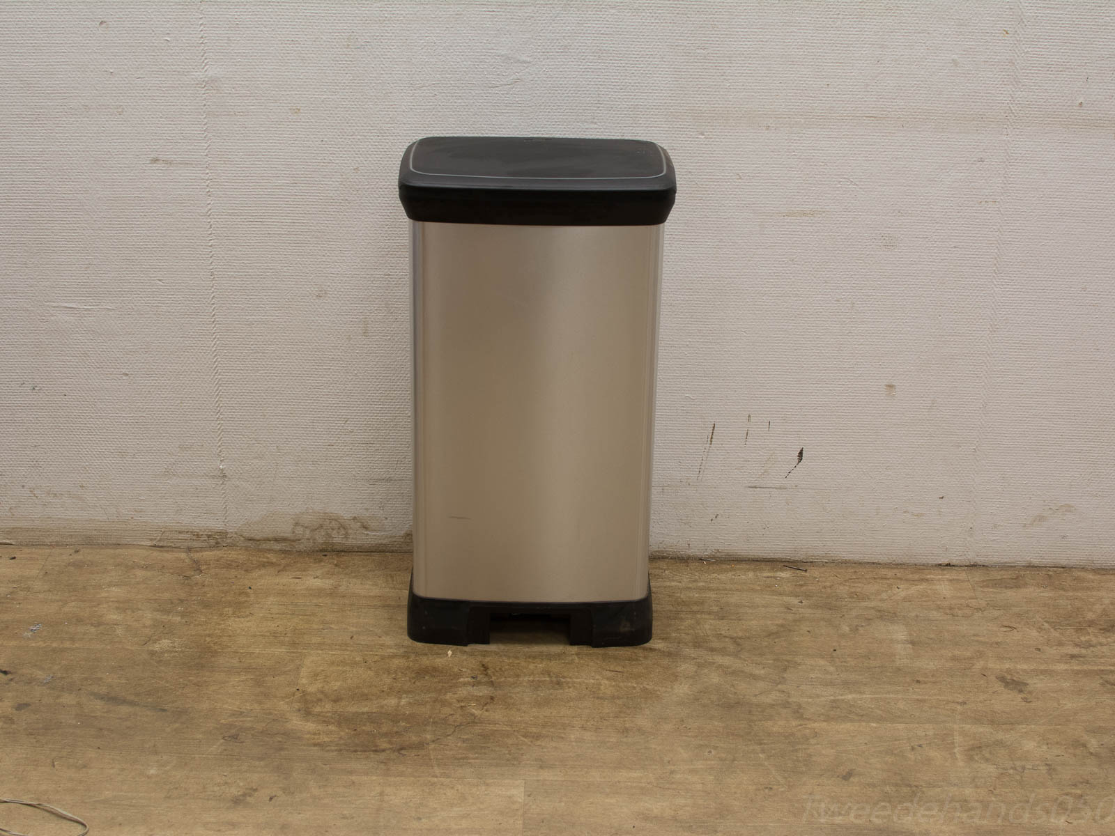 Sleek stainless steel trash can against a textured white wall, blending modern design and functionality.