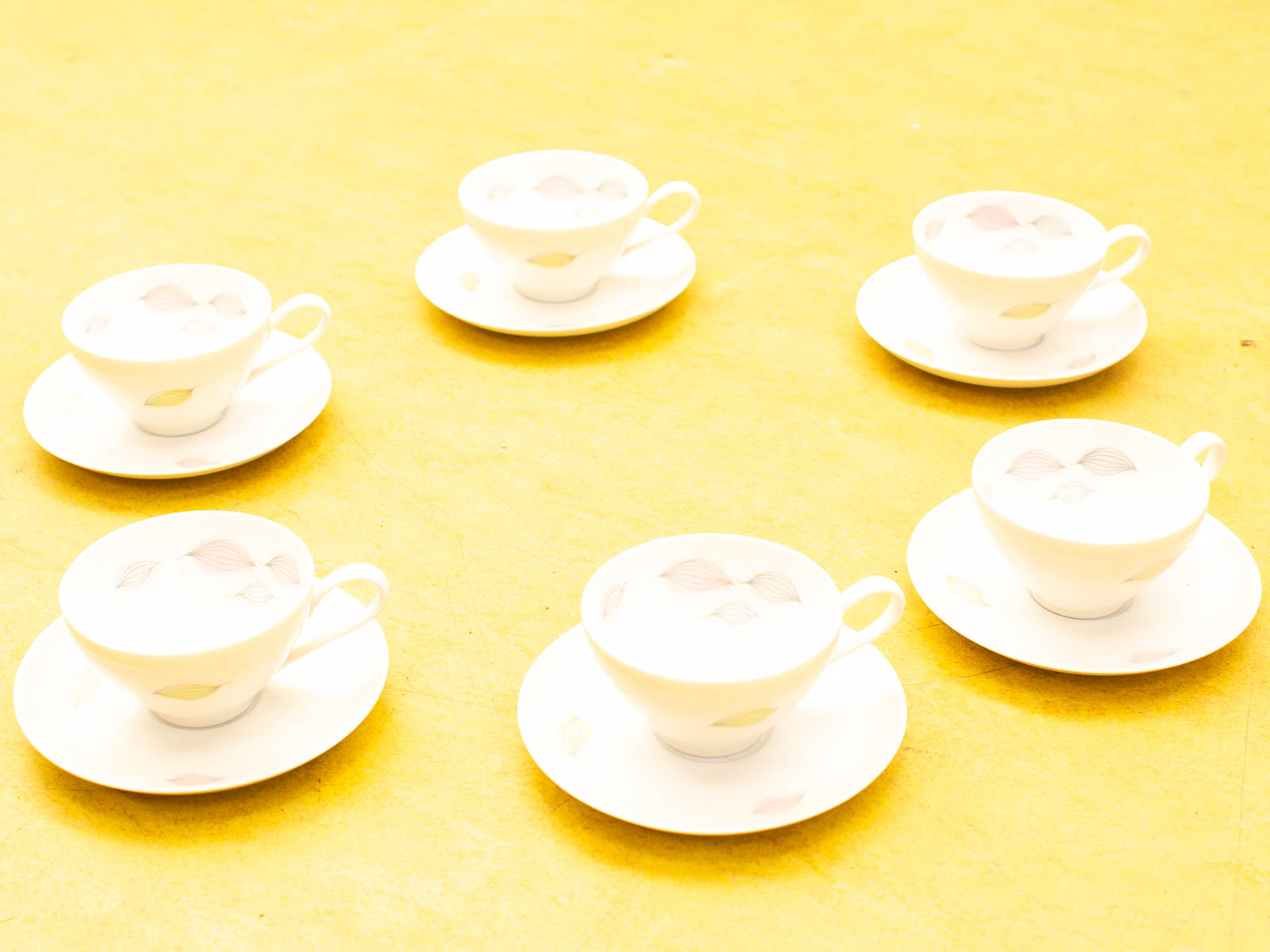 Charming porcelain tea cups and saucers against a vibrant yellow background for cozy gatherings.