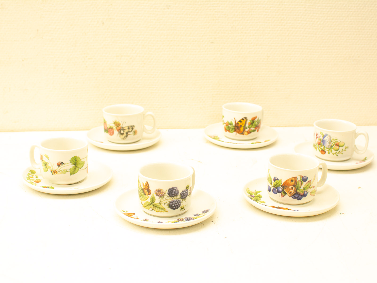 Charming vintage tea cups set with fruit and insect designs, perfect for cozy gatherings.