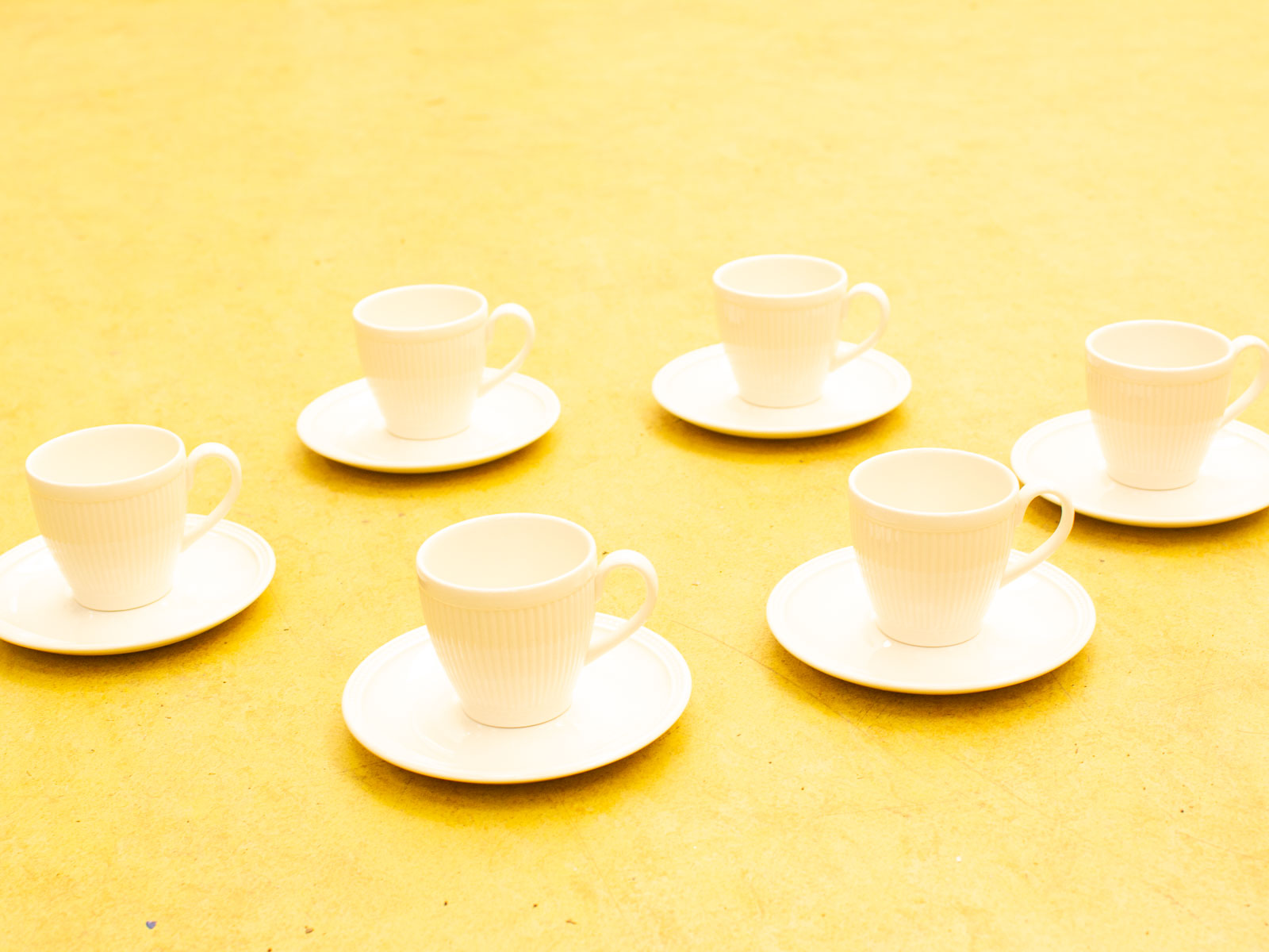 Elegant white porcelain cups and saucers on a vibrant yellow backdrop create a cheerful setting.