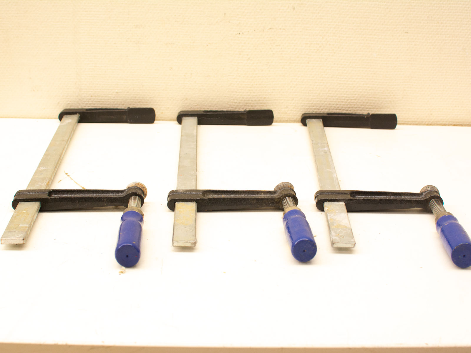 Vintage bar clamps with blue handles for precise and secure woodworking and metalworking projects.