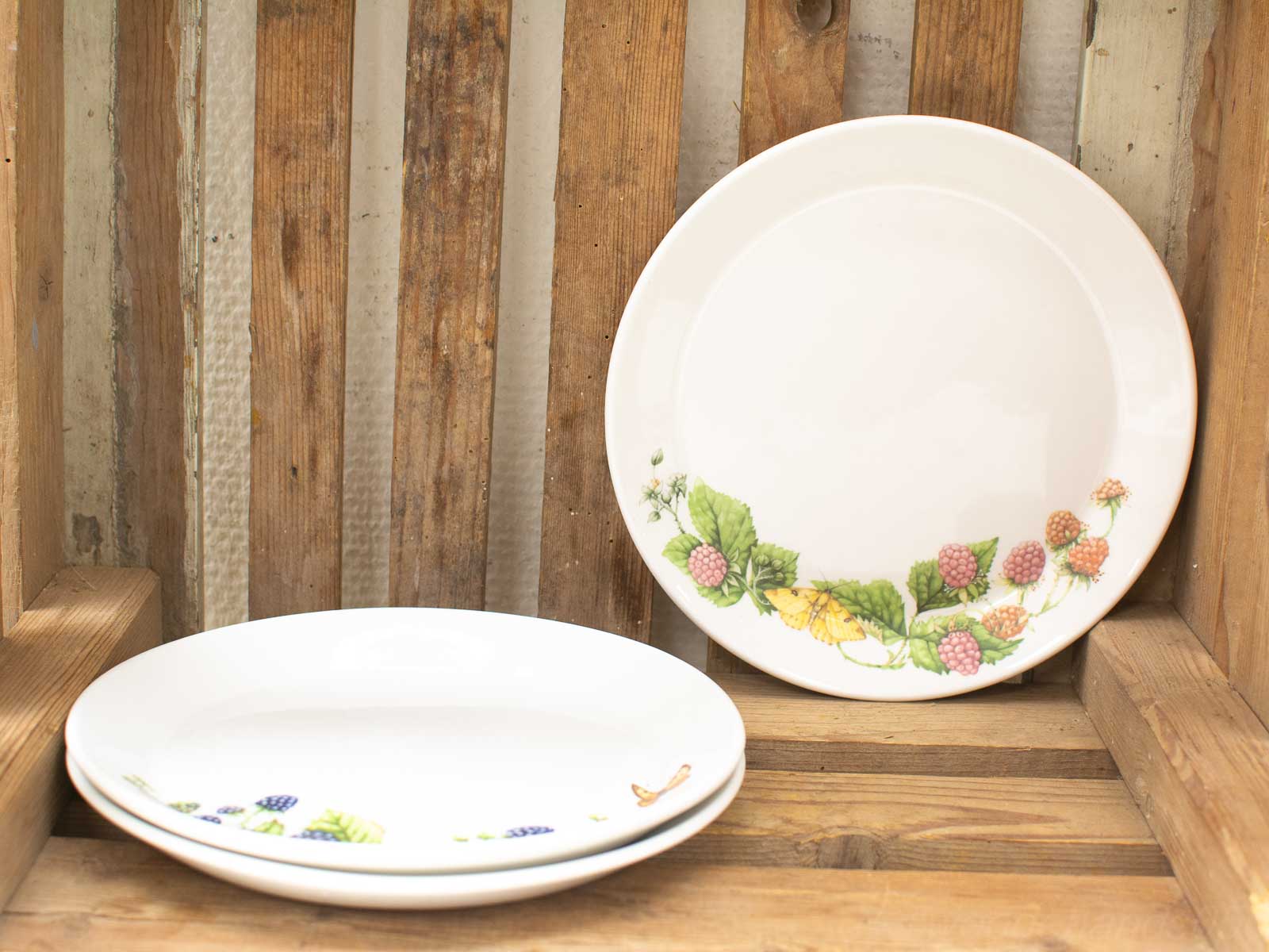 Vintage porcelain plates on a rustic wooden crate, showcasing botanical designs and farmhouse charm.