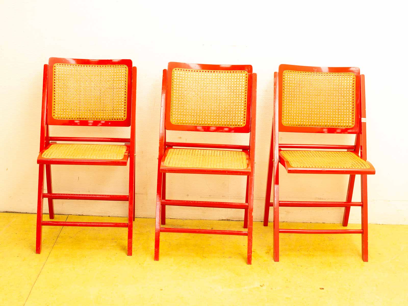 Vibrant red folding chairs with woven cane seats, perfect for stylish gatherings and decor.