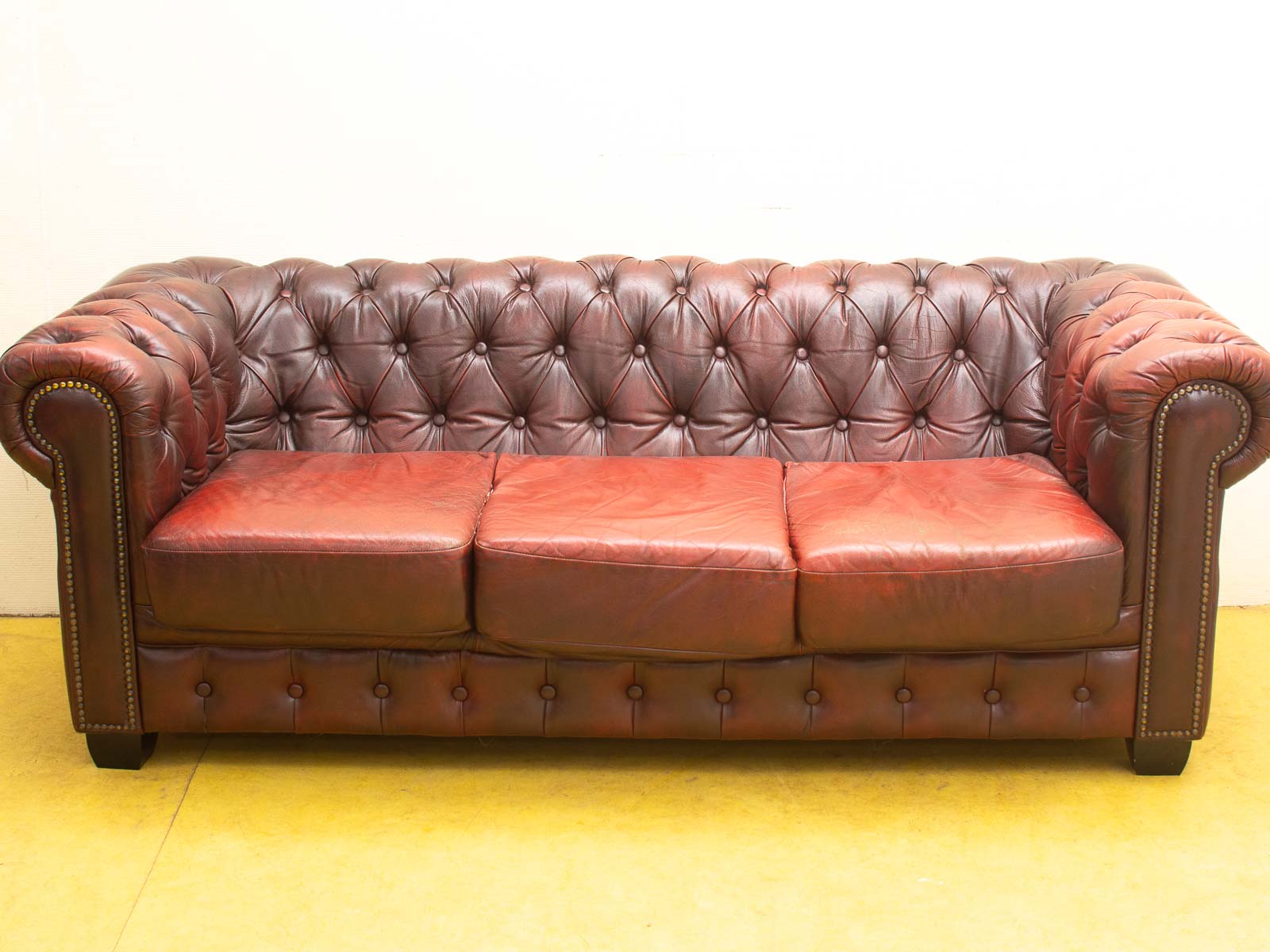 Elegant burgundy Chesterfield sofa with deep-button tufting and luxurious brass nailhead trim.