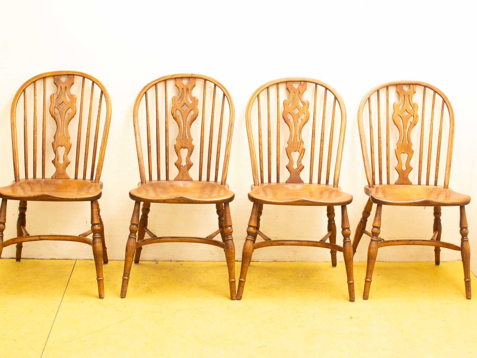 Elegant wooden chairs against a white wall, complemented by a vibrant yellow floor.