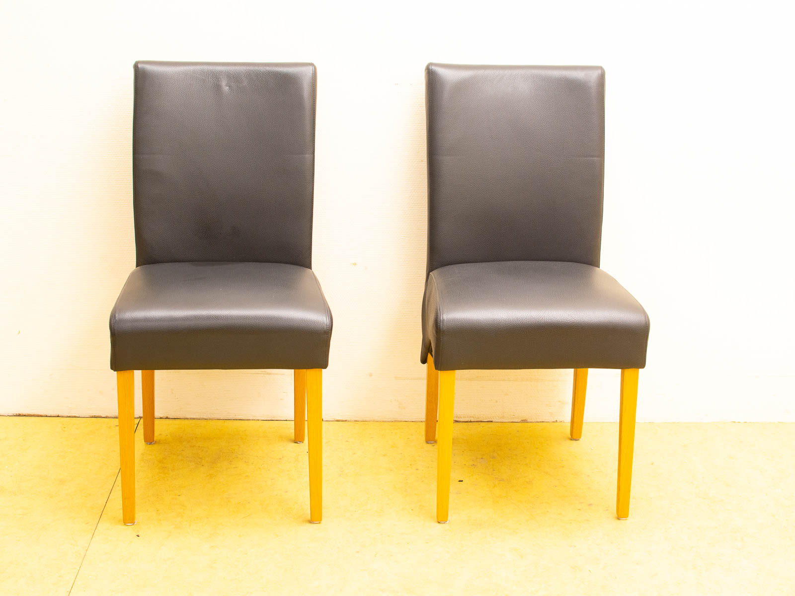 Modern black upholstered chairs with light wood legs against a white wall for stylish comfort.