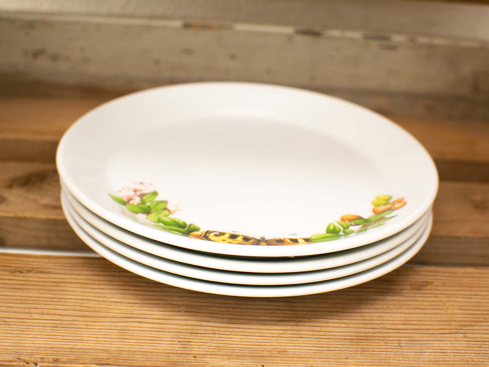 Elegant white plates with botanical design stacked on rustic wooden surface. Perfect for dining.