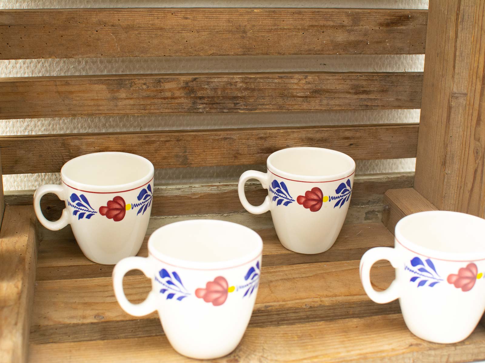 Charming floral ceramic cups on a rustic wooden shelf, perfect for cozy home decor.