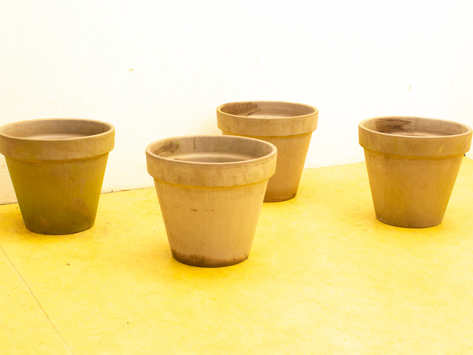 Four vintage terra-cotta pots on a cheerful yellow floor, embodying elegant simplicity and warmth.