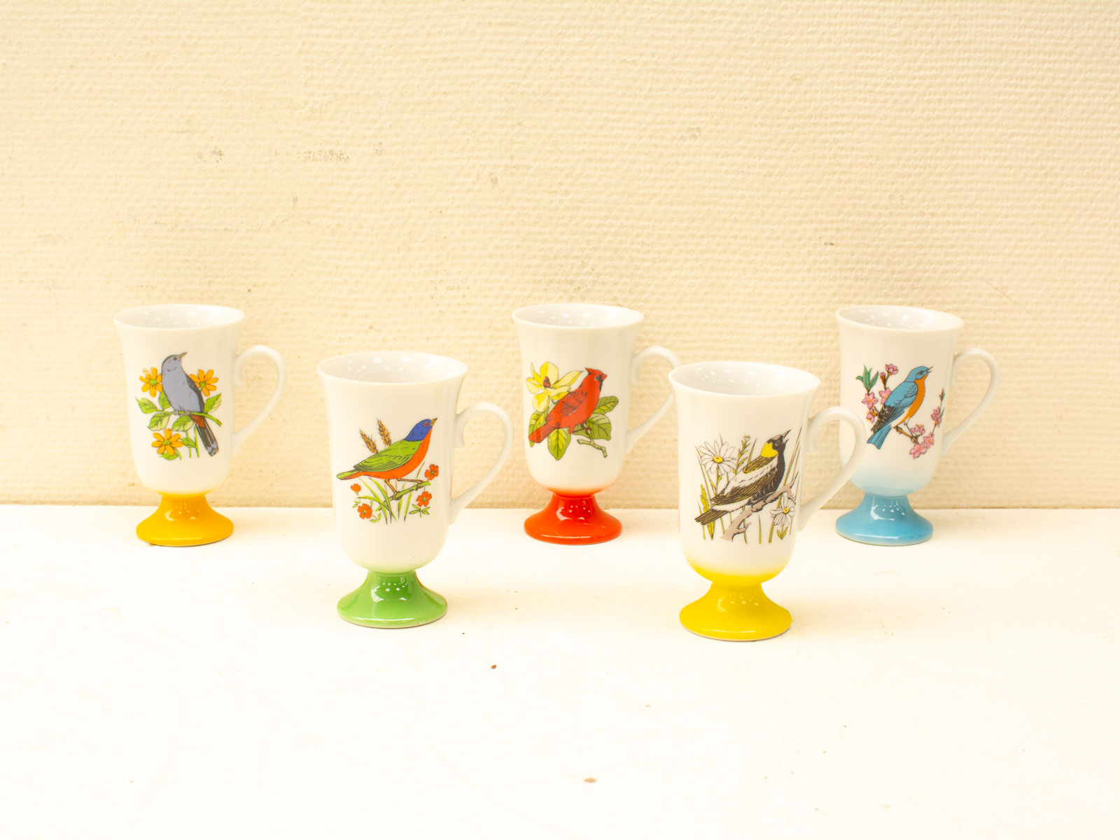 Charming decorative cups with vibrant bird designs on colorful bases for artistic tableware.