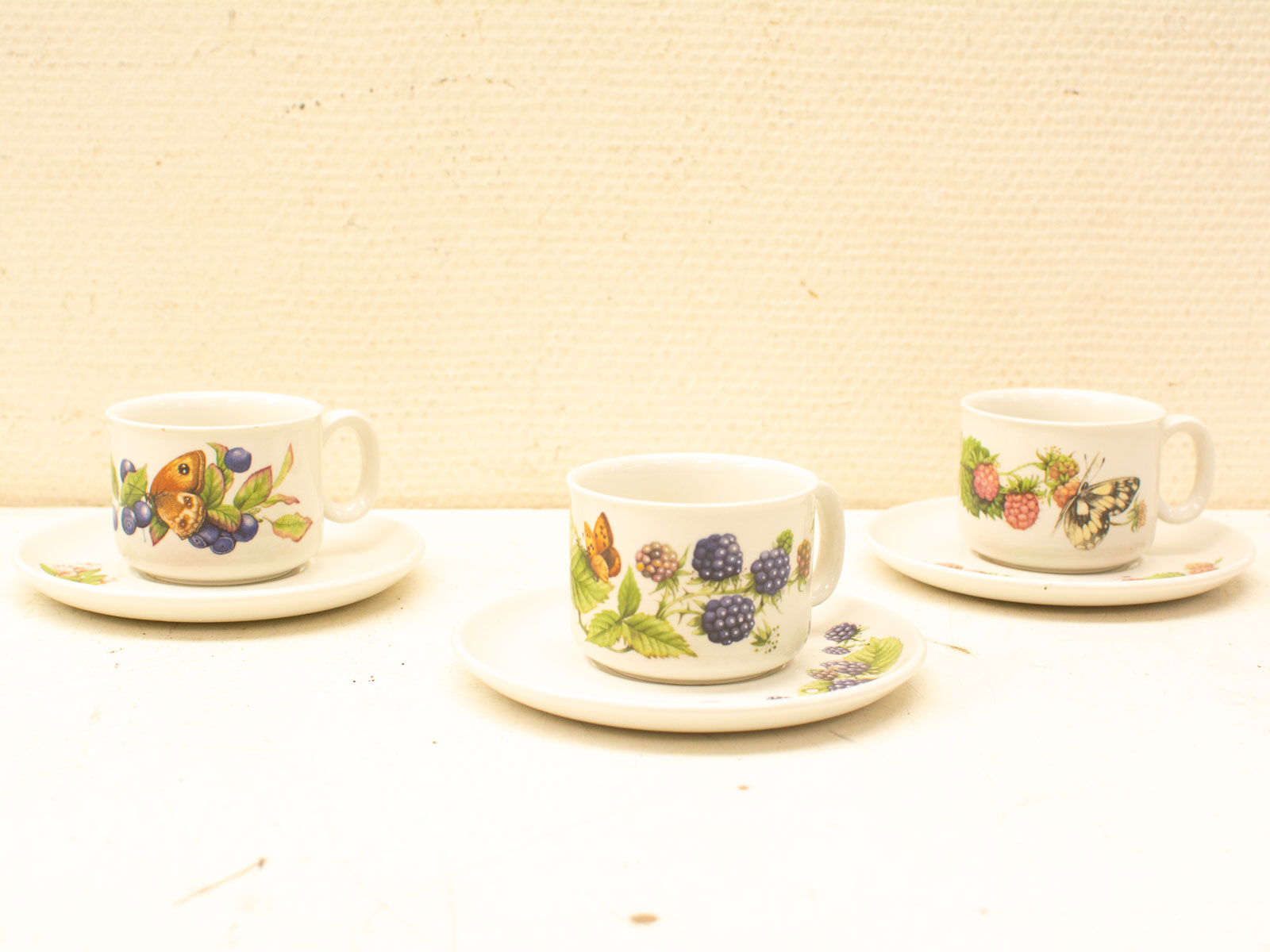 Vintage ceramic cups with fruit and butterfly designs, perfect for tea parties and decor.