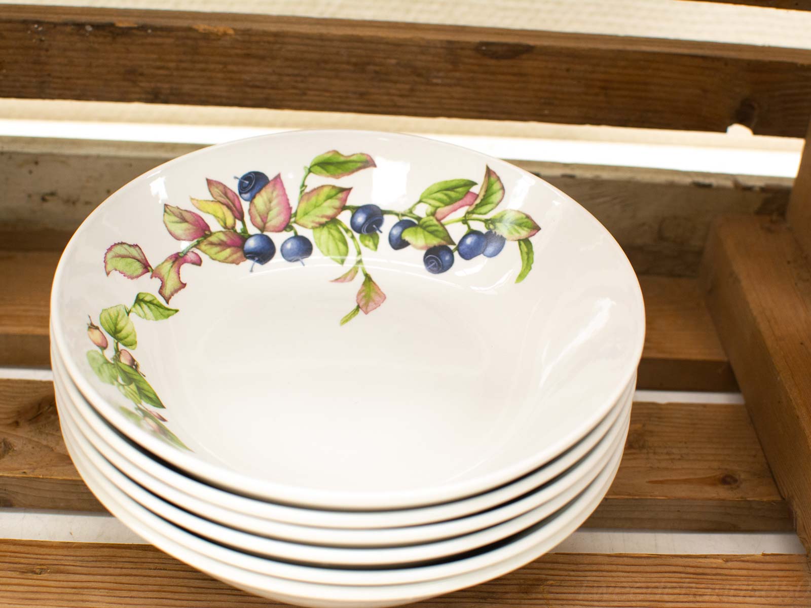 Elegant ceramic bowls with blueberry design stacked on rustic wood, perfect for dining decor.