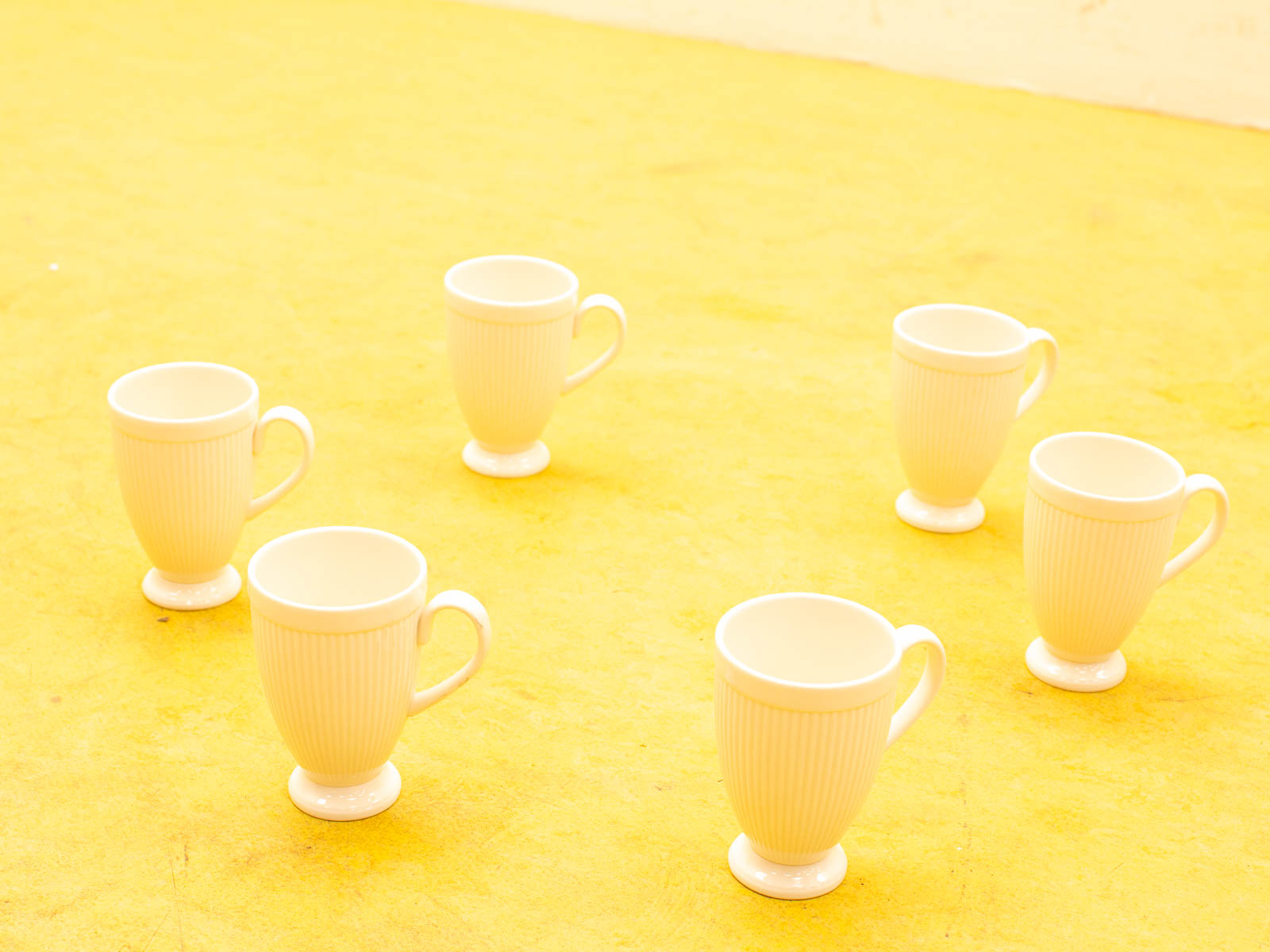 Six vintage white ceramic mugs on a bright yellow background, showcasing elegant ribbed patterns.