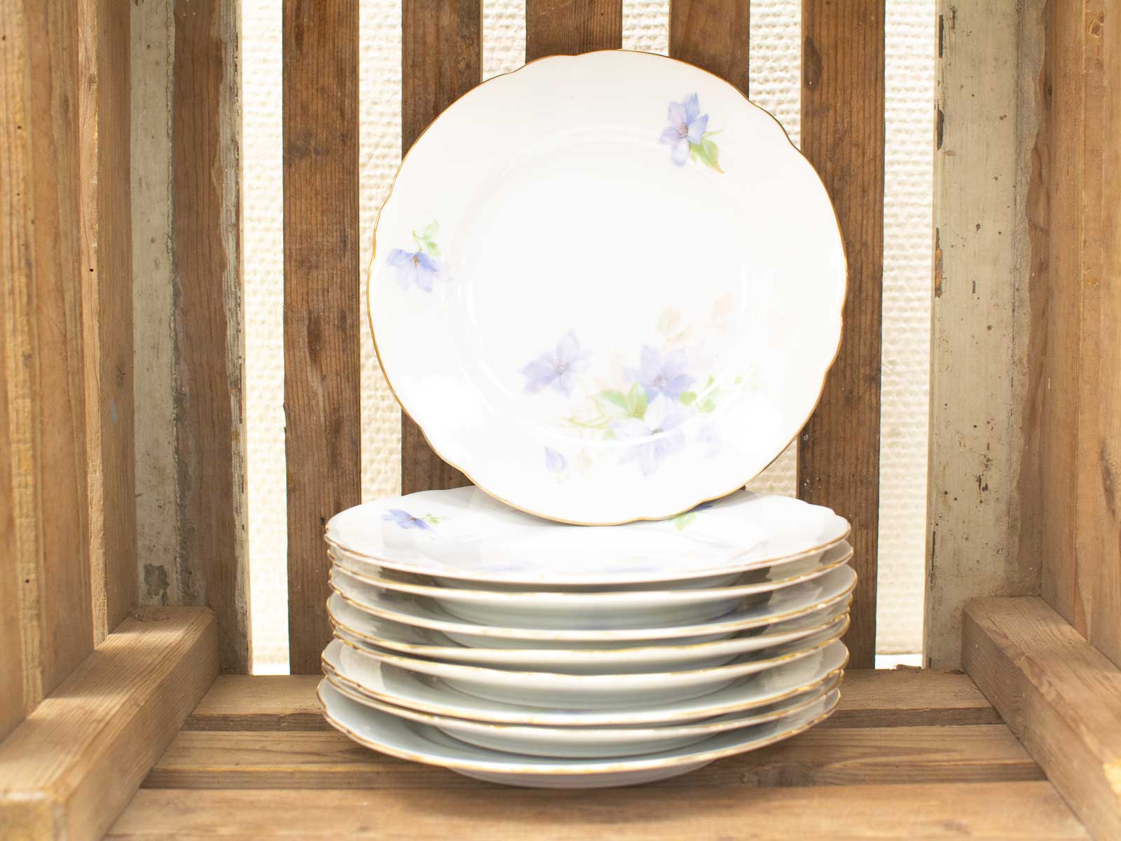 Elegant porcelain plates with floral designs in a rustic wooden crate, perfect for gatherings.