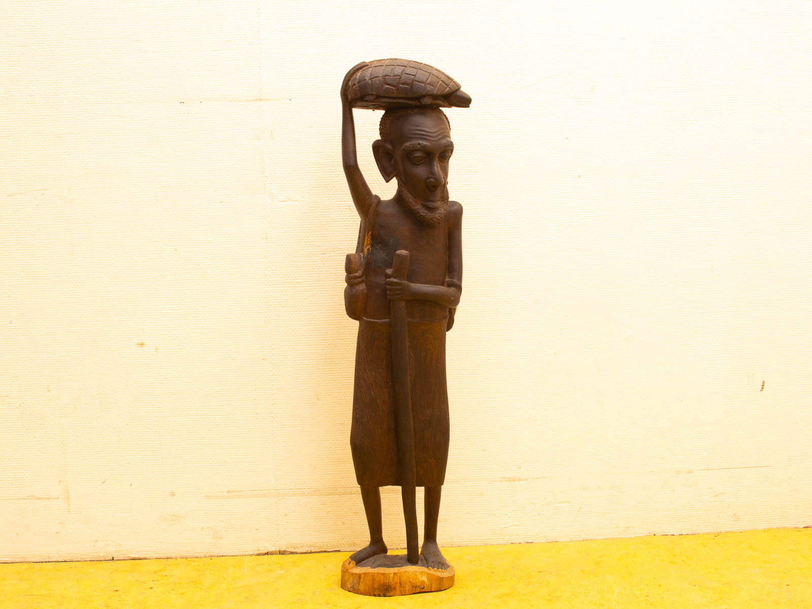 Elegant wooden sculpture of a slender figure holding a staff and turtle-like object.