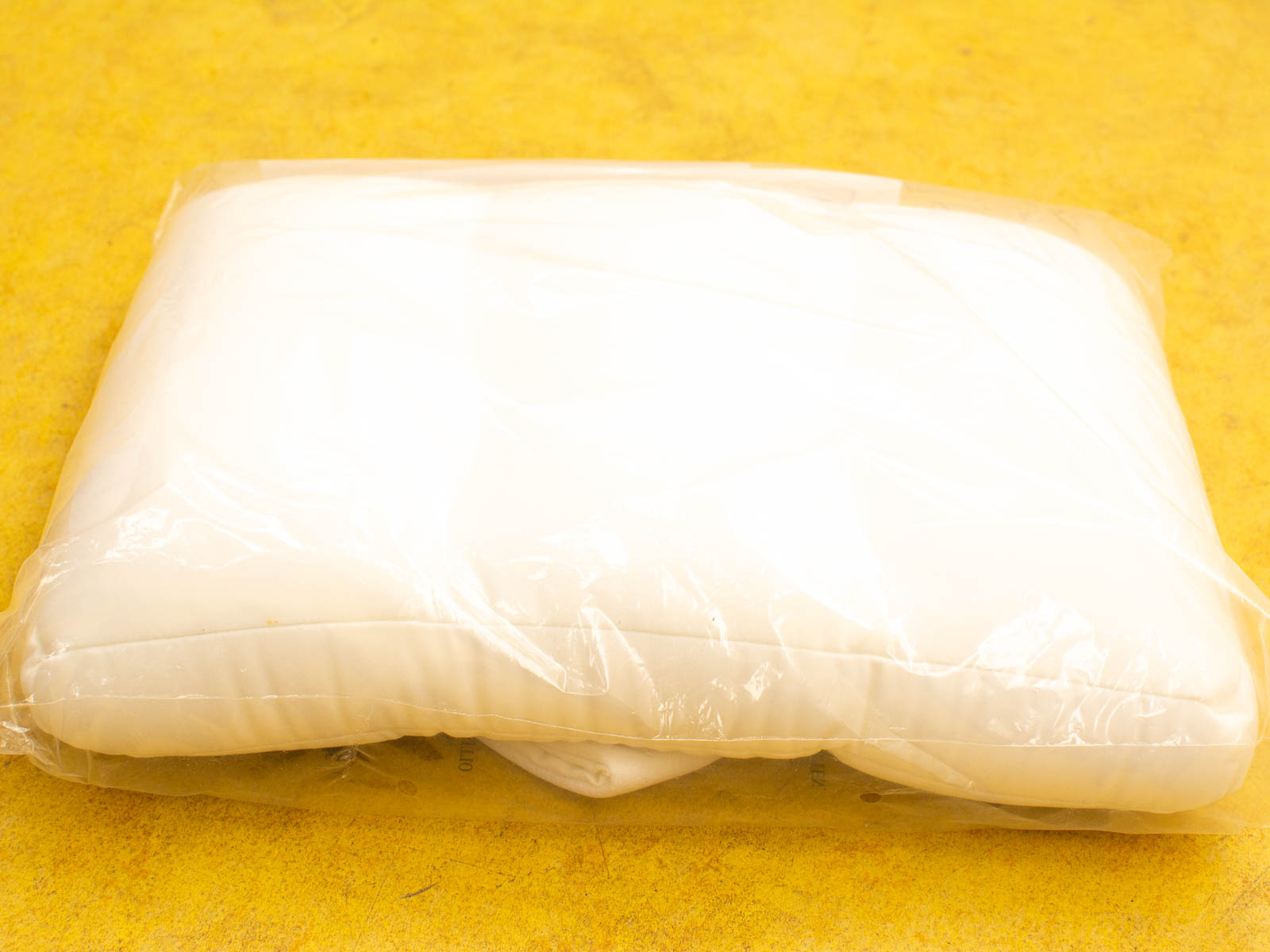 Plush white pillow in clear wrap on bright yellow background, perfect for restful sleep.