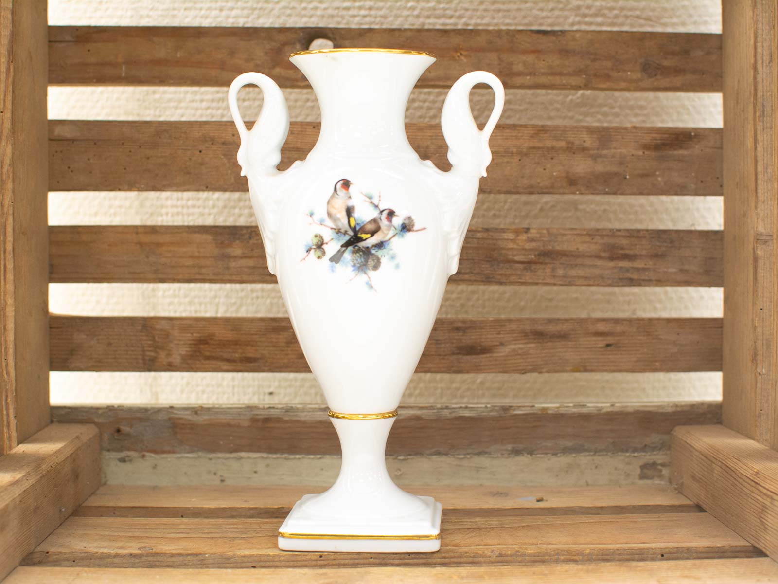 Elegant porcelain vase with bird motifs and gold trim, beautifully displayed against rustic wood.