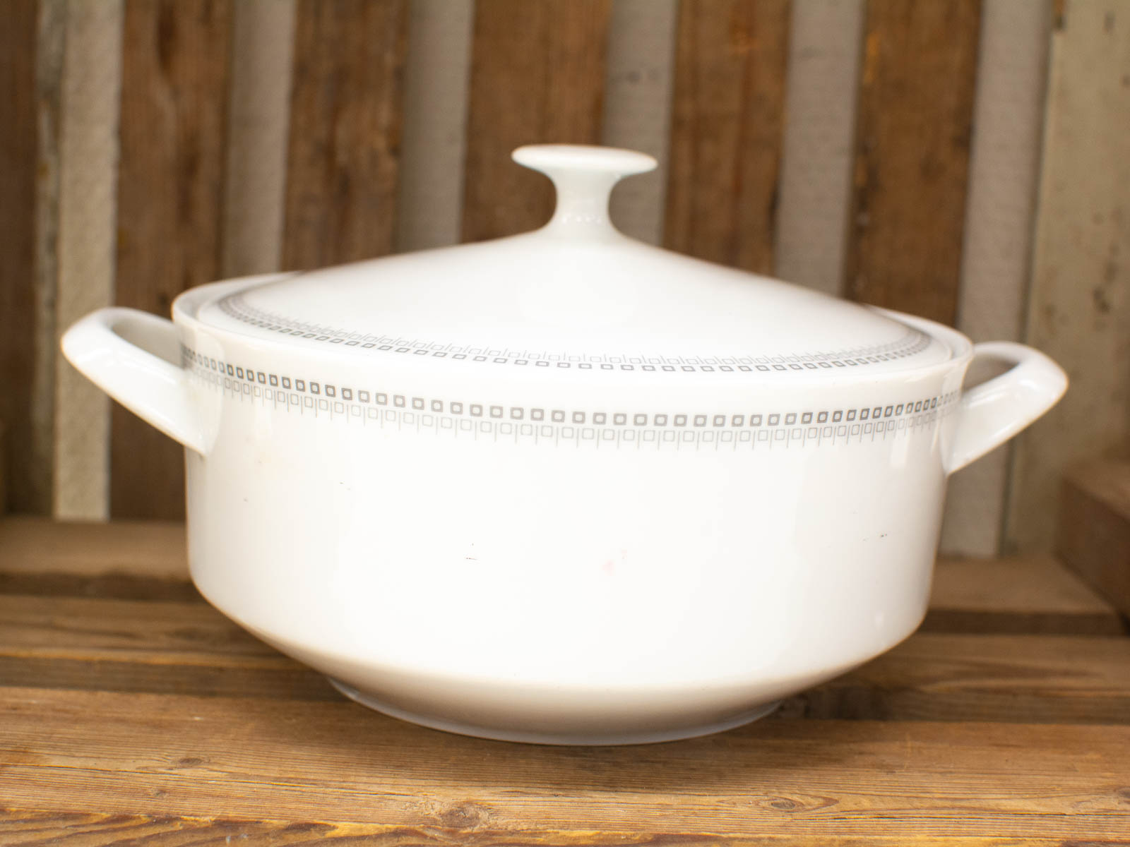 Elegant white ceramic cooking pot with lid on rustic wooden table, perfect for stylish serving.