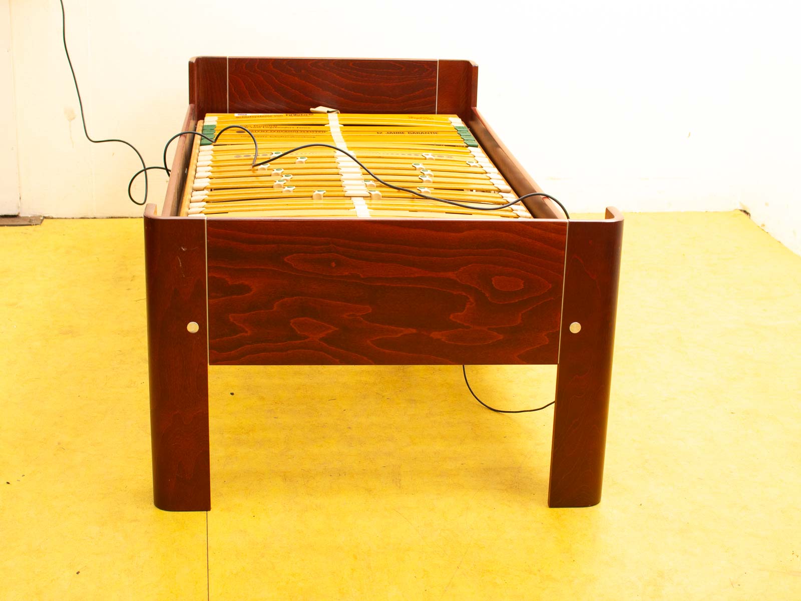 Elegant dark wood bed frame with rounded corners, slatted support, and vibrant yellow flooring.