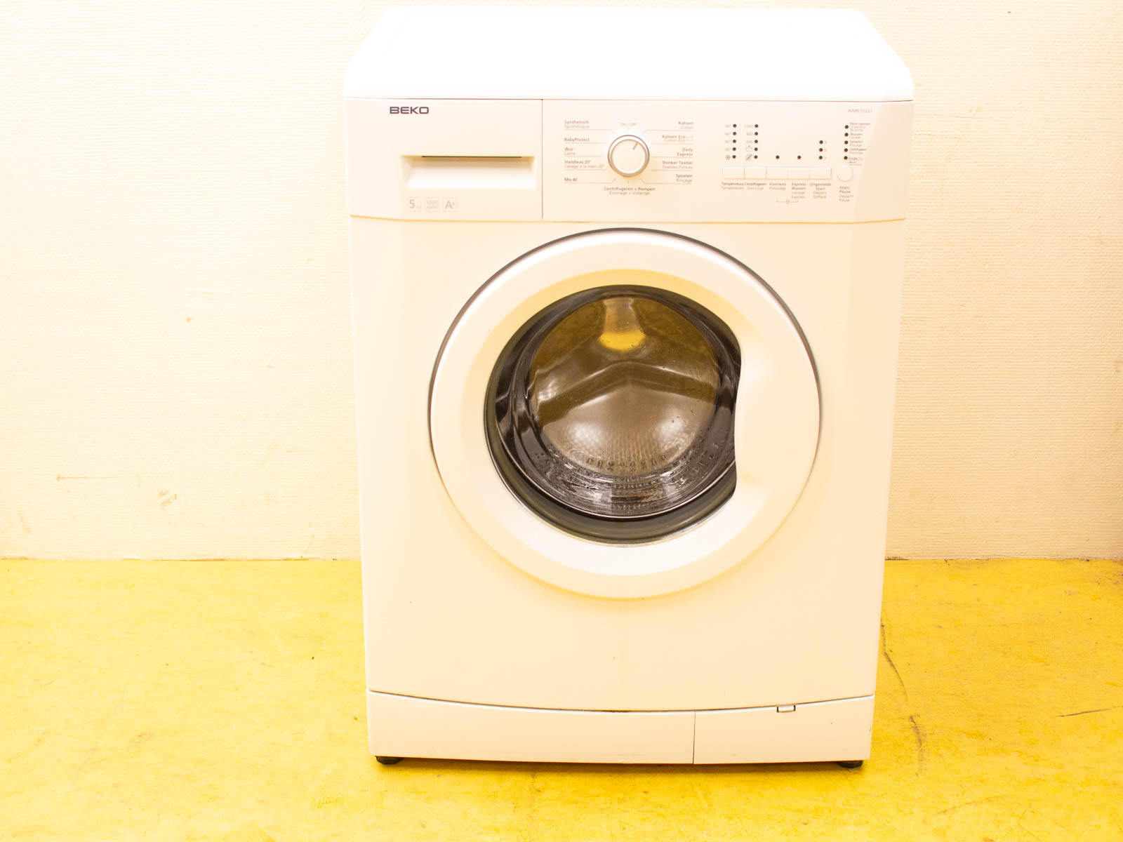 Modern Beko white front-loading washing machine with user-friendly controls on a yellow floor.