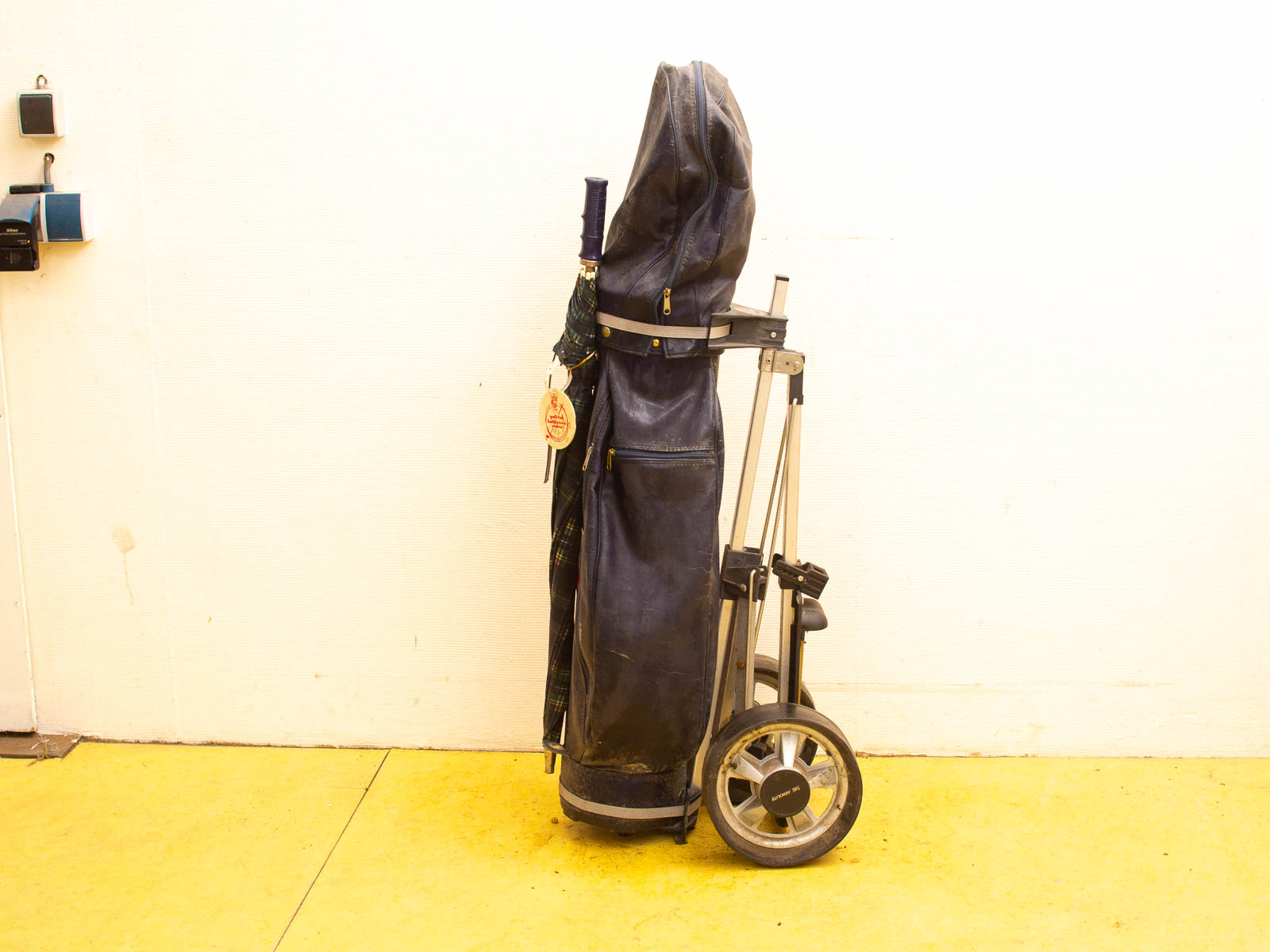 Well-worn black leather golf bag on wheels with colorful towel, ready for the course.