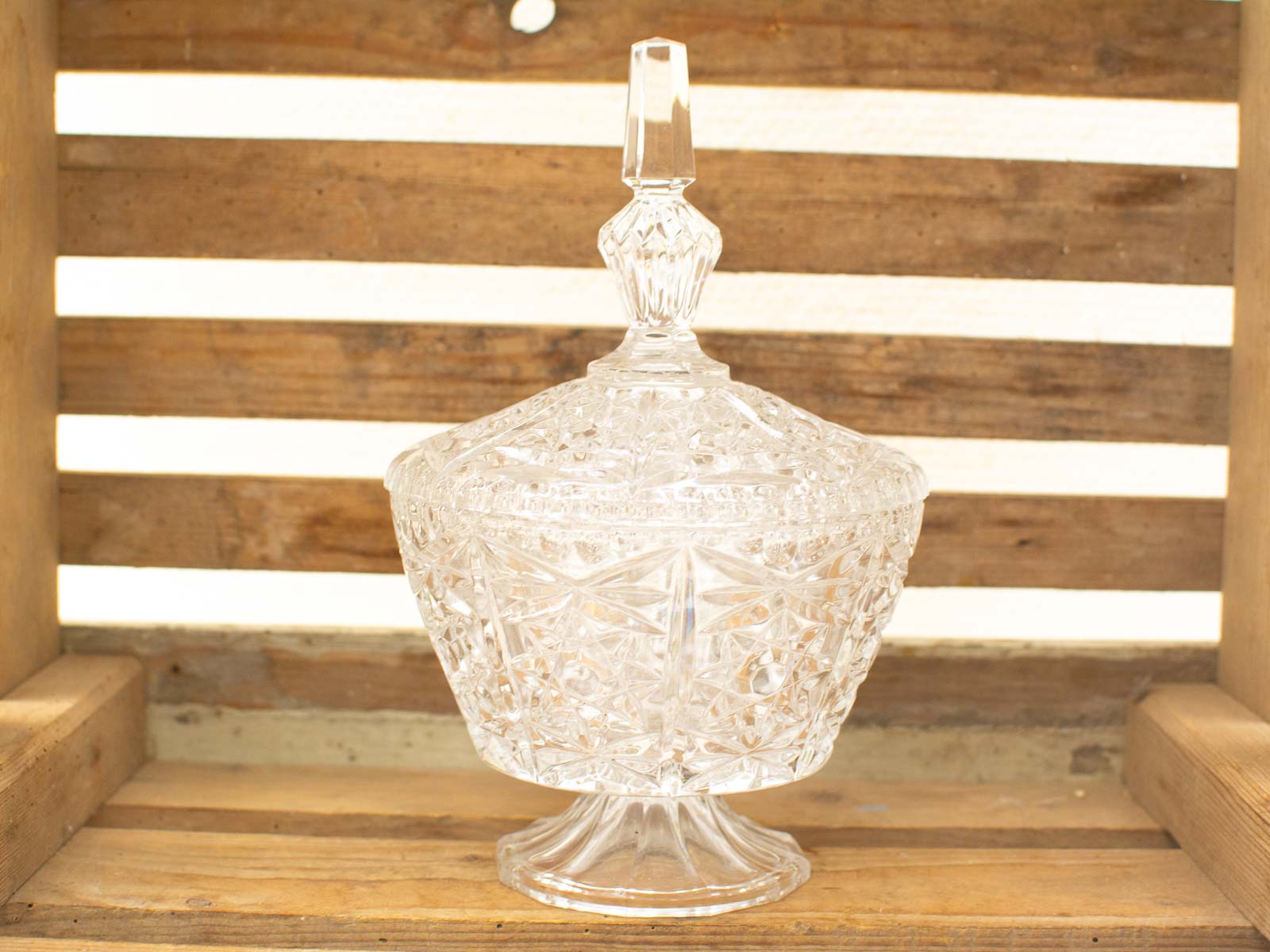 Elegant crystal compote with lid, showcasing geometric designs on rustic wooden surface.