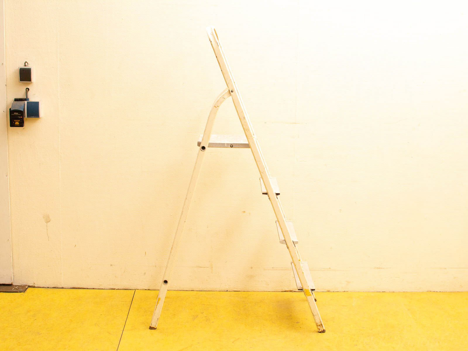 White metal step ladder in a cheerful yellow workspace, ideal for everyday tasks and repairs.