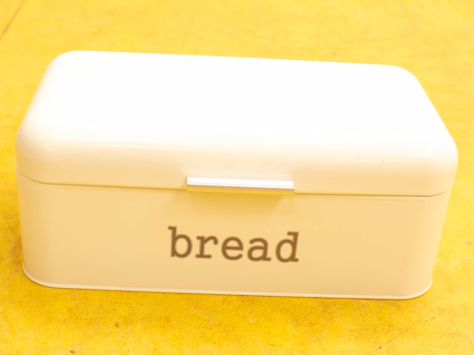 Vintage cream bread box with glossy finish, vibrant yellow background adds charm to kitchens.