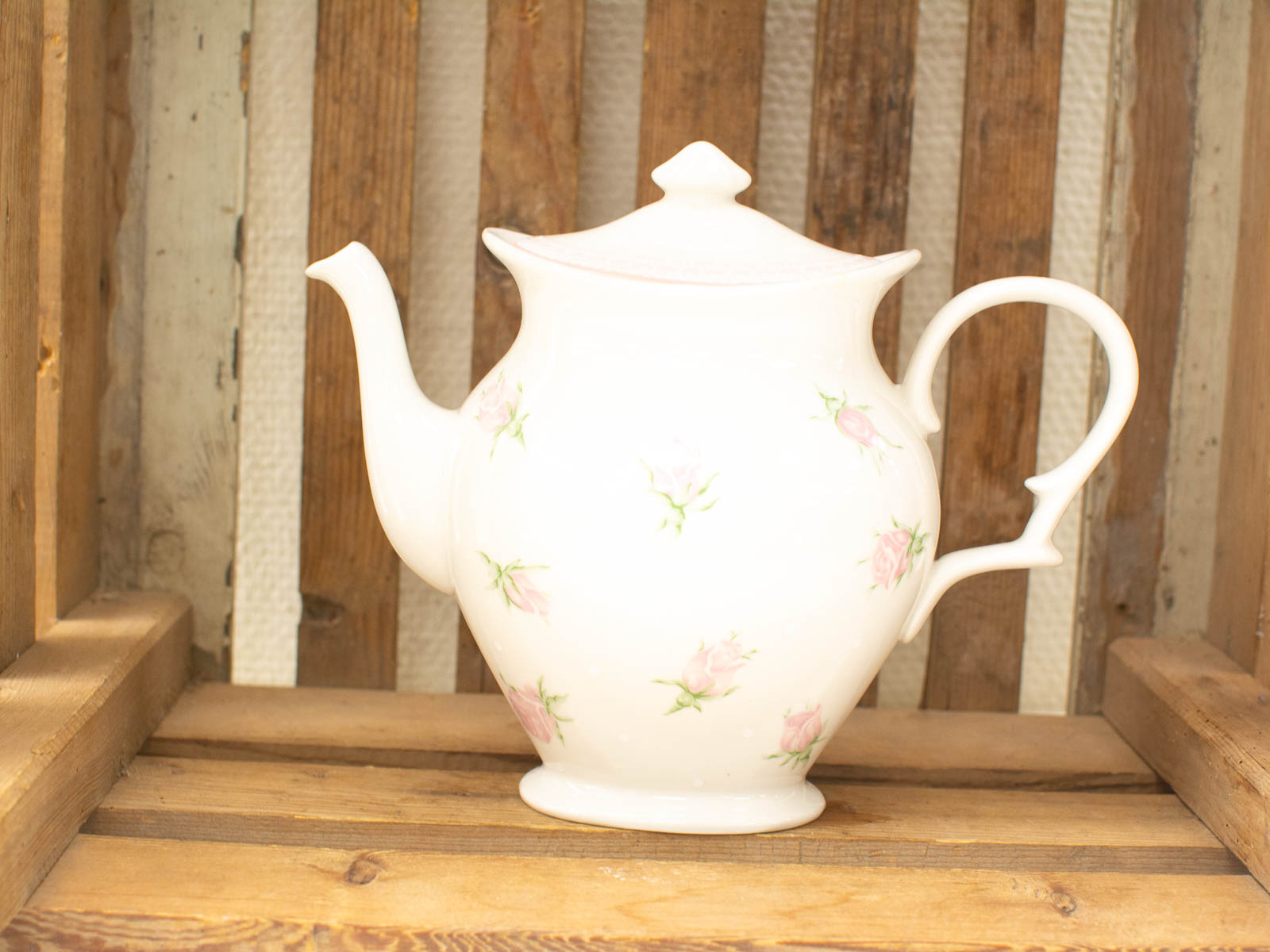 Elegant porcelain teapot with pink roses on a rustic wooden surface, perfect for tea parties.