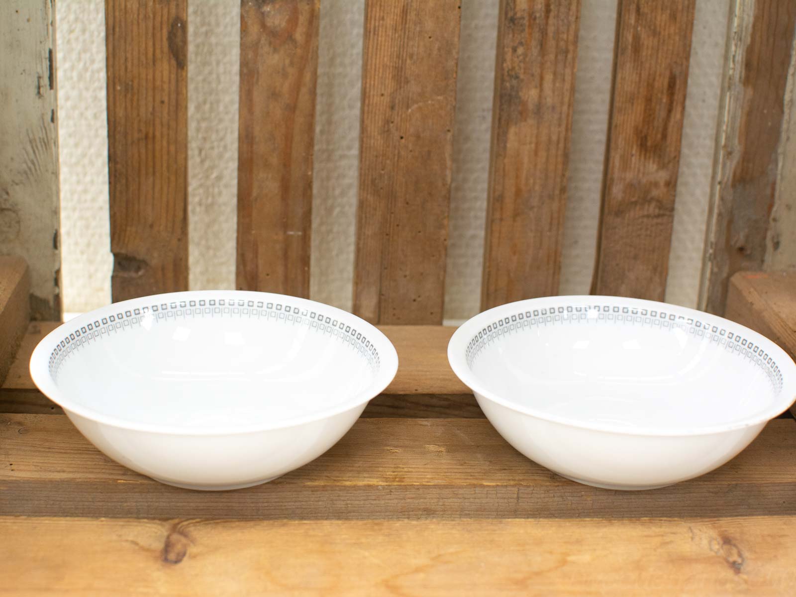 Elegant white ceramic bowls on rustic wooden table, enhancing warm dining atmosphere.