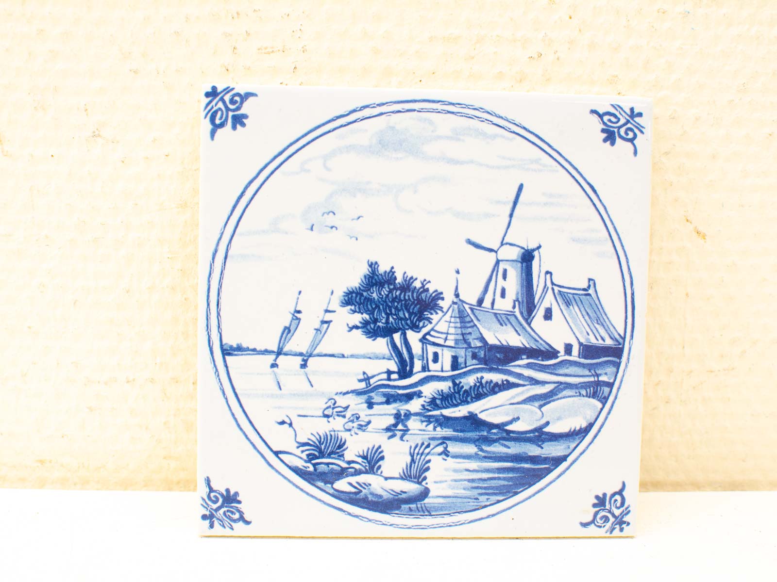 Charming blue and white ceramic tile depicting a tranquil Dutch landscape with windmills and waterway.