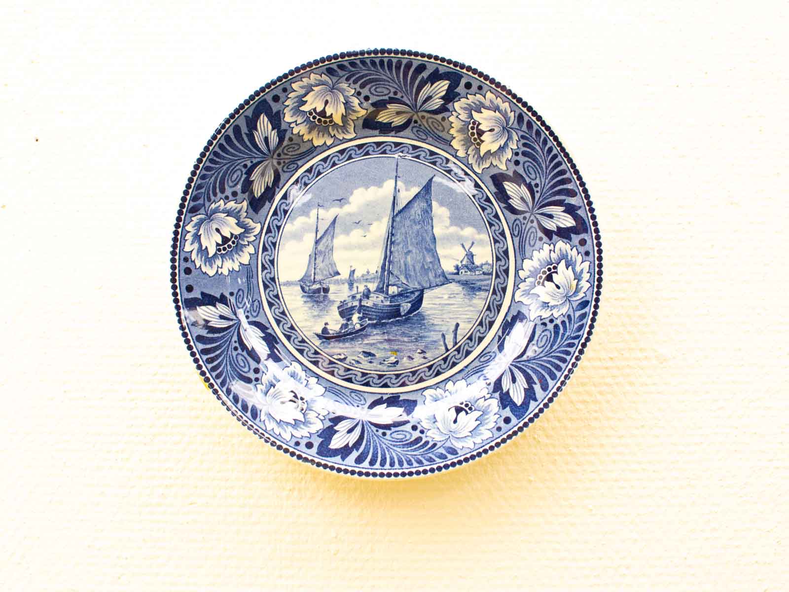 Elegant blue and white decorative plate showcasing a serene maritime scene with floral accents.