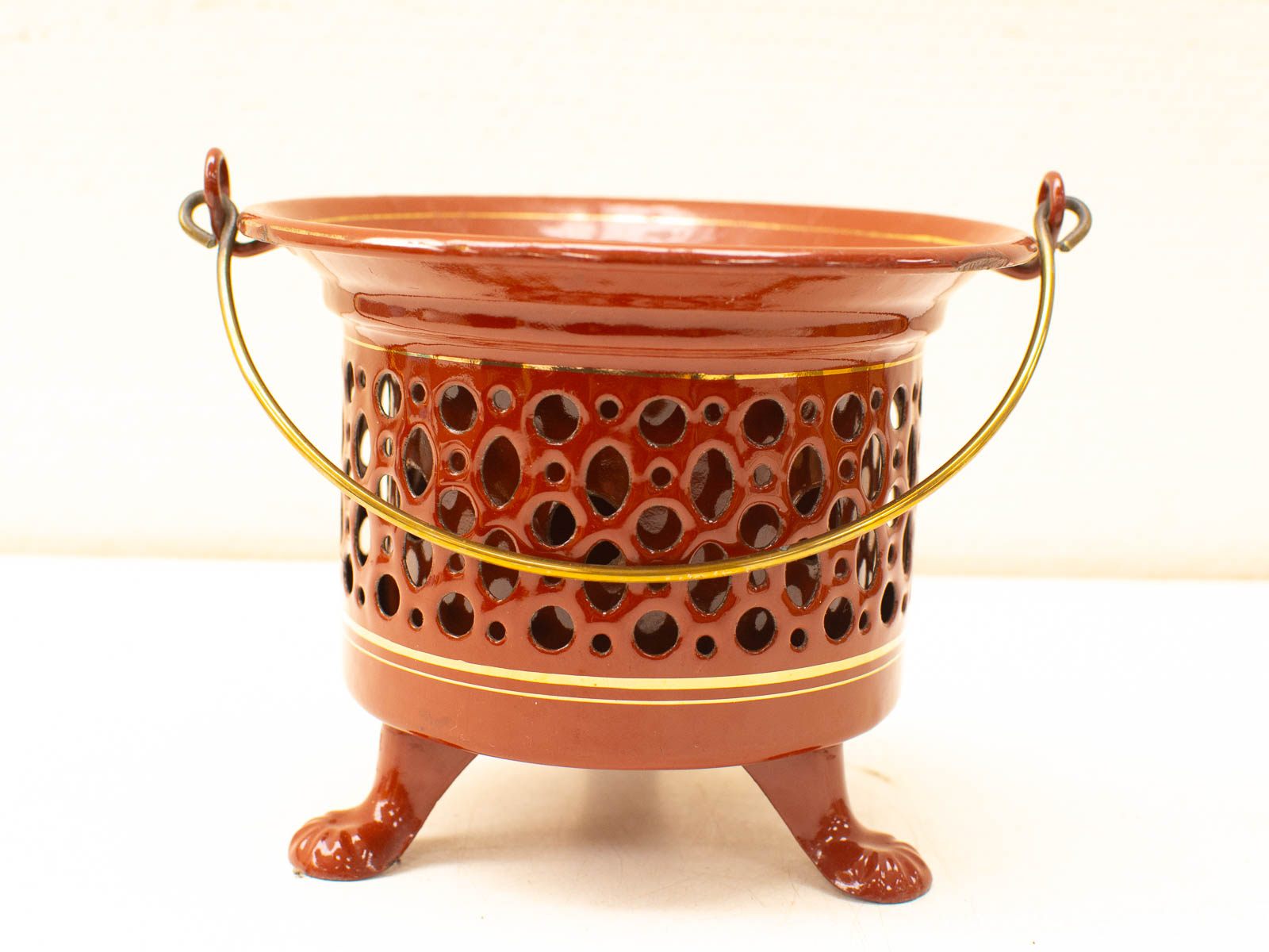 Elegant reddish-brown ceramic bowl with intricate cutouts, brass handle, and sturdy feet for versatile use.